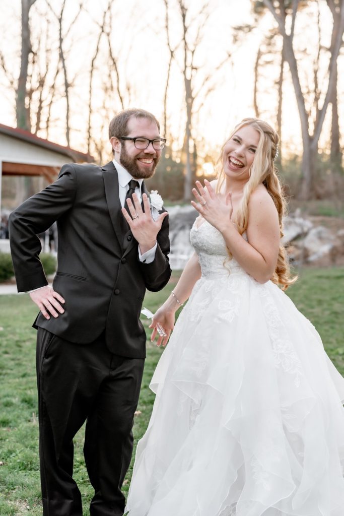  a bride and groom laughing as they hold their hands out to reveal their wedding rings