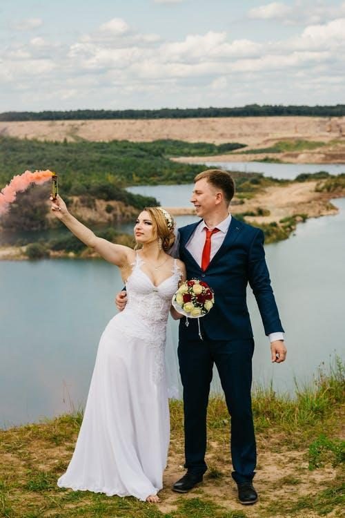 a bride and groom posting in front of a lake and popping a powder cannon